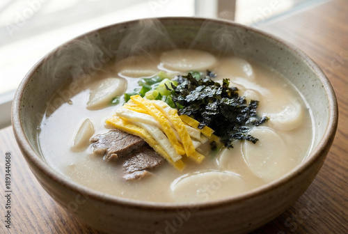 Traditional Korean New Year food Tteokguk rice cake soup with beef, egg and seaweed garnish in ceramic bowl with steam
