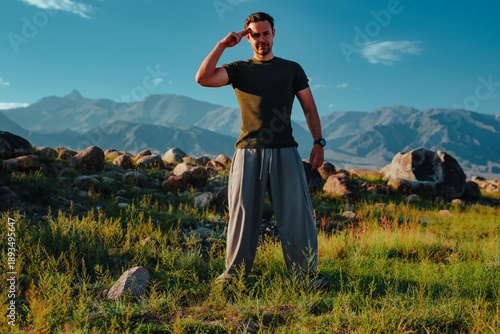 Athletic young man saluting outdoors with mountains in background