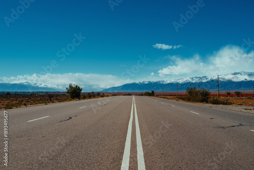Lonely road with double solid line on sunny day with mountains