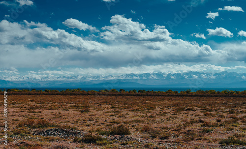 Steppe view of Kyrgyzstan with mountains, lake and clouds on bright sunny day
