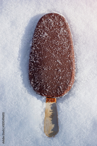 Chocolate coated popsicle ice cream in snow. The frozen sweet dessert in closeup view.