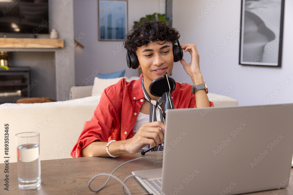 Fototapeta premium Man wearing shirt and headphones speaking into microphone in living room with laptop and water