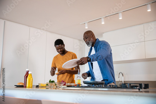 African american father, son cooking at home kitchen island stirring vegetables in frying pan