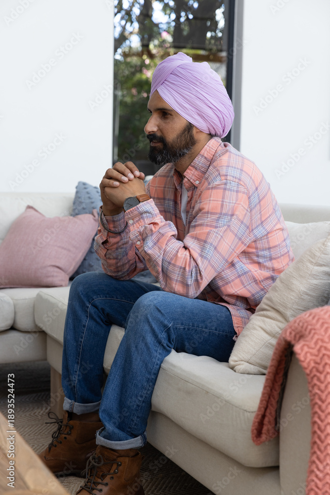 Obraz premium Indian man with turban sitting on sofa in living room looking through window