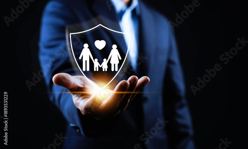 Family insurance protection concept with shield icon and parents holding children symbol in businessman hand, representing life insurance, healthcare coverage, financial security.