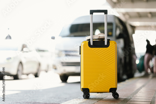 Fotografía A bright yellow rolling suitcase stands at a transport pickup area with vehicles in the background, symbolizing arrival, departure, and modern urban travel lifestyle