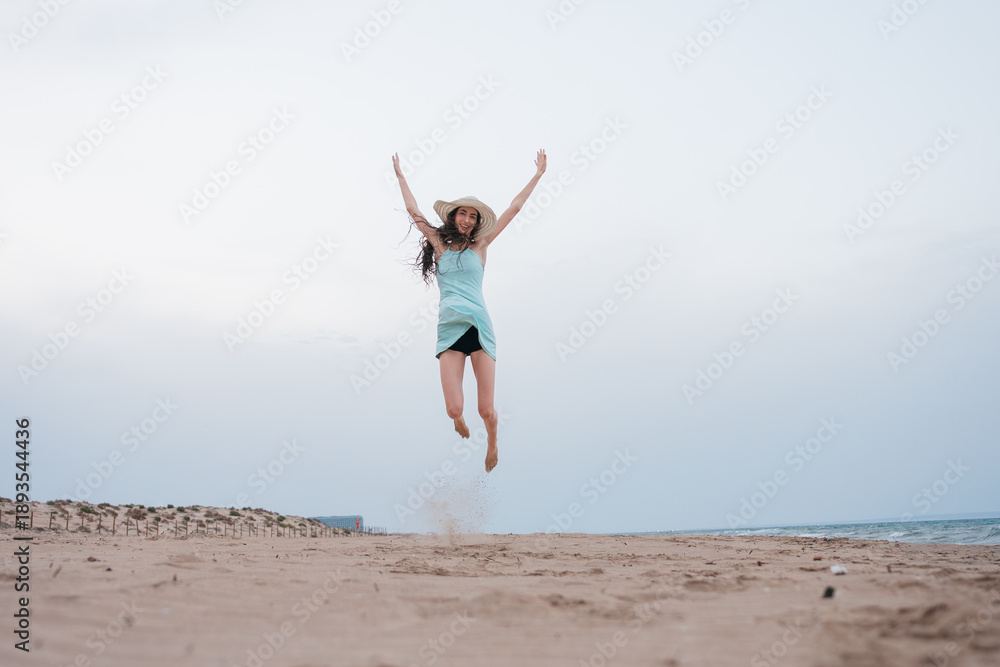 Obraz premium Young woman jumping with joy on summer beach