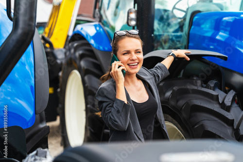 Картината върху платно Female agribusiness executive talking on mobile phone by new tractor at at agric
