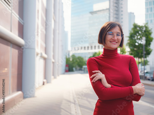 Free Download Woman in glasses and red turtleneck, dressed in business style, stands in center of Frankfurt, surrounded by modern buildings and urban life, embodying professionalism and confidence - GFXLoad