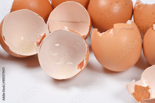 A close up side view of several empty and broken brown eggshells resting on a plain white surface after being used for cooking