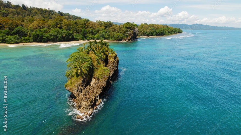 Obraz premium Rocky palm covered islet off lush tropical Caribbean coastline in Costa Rica.