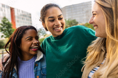 Three happy multiracial young women laughing outdoors. United female best friends having fun walking in city street. Community and international friendship concept