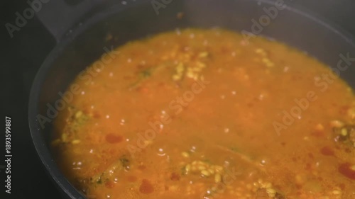 Hand lifting glass lid from pot with boiling rice stew on stove