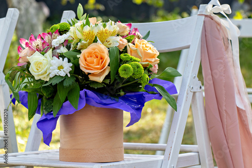 A bouquet of flowers in a wooden vase on a white chair..