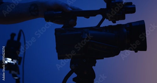 Close up silhouette of hands operating a professional video camera against a blue background. Backstage photo shoot.
