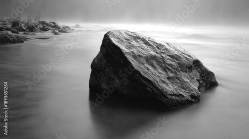 A solitary rock rests in serene, smooth water, shrouded by soft, hazy light