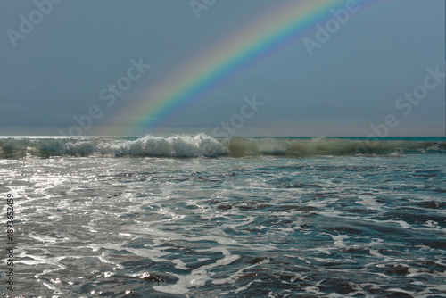 Breaking sea waves and foamy surf on a sandy beach with dramatic storm clouds and blue sky. Scenic seascape background, nature and travel concept.