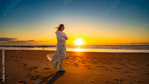 Beautiful middle-aged woman enjoying walk on sandy beach on sunset on windy spring day. Side view. Monte Clerigo beach on Algarve coast in Portugal 