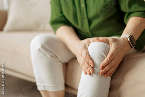 Billede på lærred Close up of elderly caucasian woman holding knee while sitting on sofa at home,