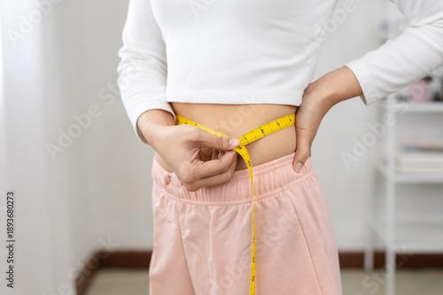Obraz na plátne women measuring her waist with tape measure, symbolizing weight loss, fitness progress, body care or diet tracking