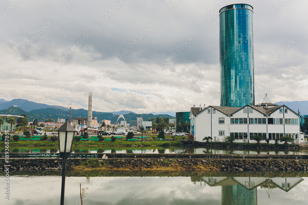 Obraz premium Tranquil city reflections cape with mountains. Peaceful waters mirror modern buildings and nature. Calm water perfectly reflects skyline with scenic mountain background