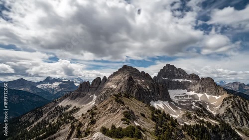 Stunning time lapse sequence of a rugged mountain range in the alps. Panoramic view of rocky peaks with snow and dynamic clouds moving across the blue sky