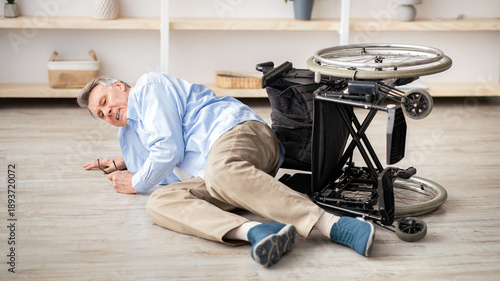 Принти на полотні A senior man with gray hair is lying on the floor after his wheelchair has tipped over in a cozy living room