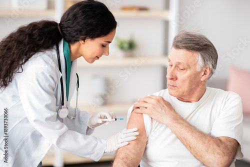 A nurse is administering a vaccination to a senior man in a clinic. The man looks attentive as the nurse prepares the injection. The setting is bright and welcoming, suitable for healthcare.