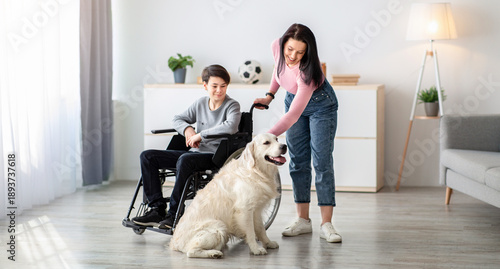Wallpaper Mural A boy using a wheelchair interacts with a friendly dog while a girl gently pets the dog. They are inside a well-lit room with simple furniture, creating an inviting atmosphere. Torontodigital.ca