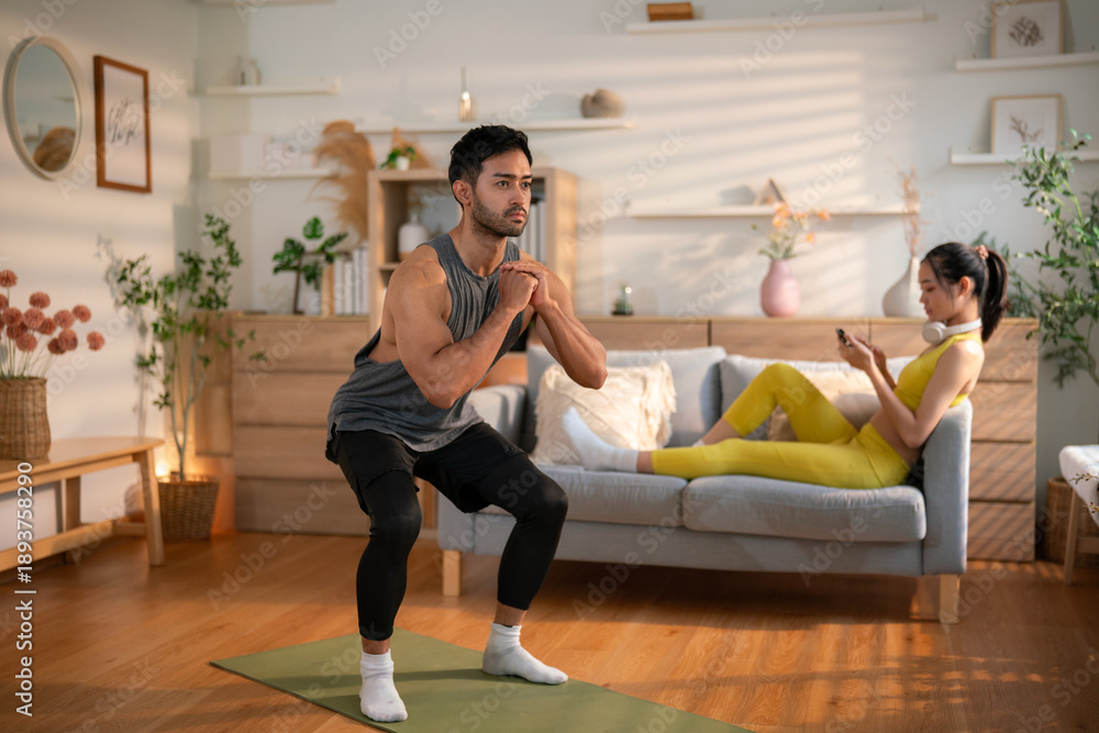 Obraz premium Man doing squat exercise while woman relaxes on sofa 