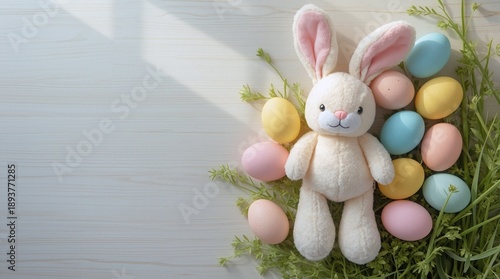 A plush bunny with pink ears sits among pastel eggs and greenery. The arrangement includes blue, yellow, and pink eggs on a light wooden surface.