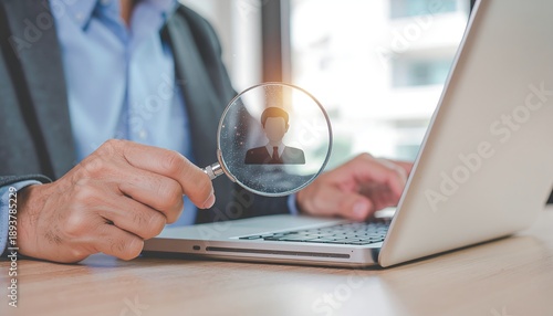 Businessman holding magnifying glass over a laptop screen with a candidate icon, recruitment concept