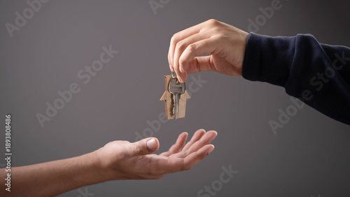 Hand giving house keys with wooden home keychain to another hand, symbolizing real estate deal, property handover, home ownership, buying house, mortgage approval, trust, and housing business concept.