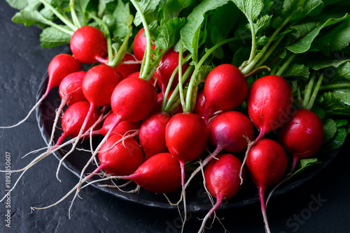 Fresh washed radishes on black plate against dark background. Minimalist food styling for organic vegetables and modern kitchen concept