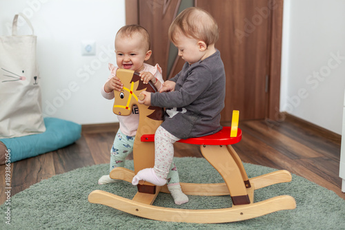Wallpaper Mural Two adorable babies playing on wooden rocking horse indoors, happy toddlers sharing toy in cozy nursery, childhood friendship Torontodigital.ca