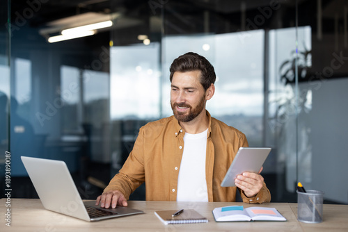 Person working on a laptop and holding a digital tablet, navigating multiple screens for efficient remote work and productivity in a contemporary business environment