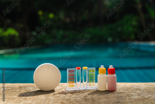 Fotografija Pool water testing kit with chlorine tablet and reagent bottles on pool edge fo