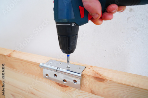 Wallpaper Mural Screwdriver is used to attach hinge to wooden door frame. Cordless drill to secure silver hinge to wooden door. Installing doors in room of an apartment or house. Installing Doors use screwdriver. Torontodigital.ca
