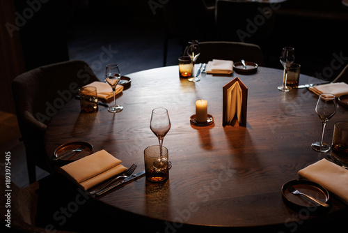 Detail of an interior of a restaurant with wine glasses and a table, napkins and candles.