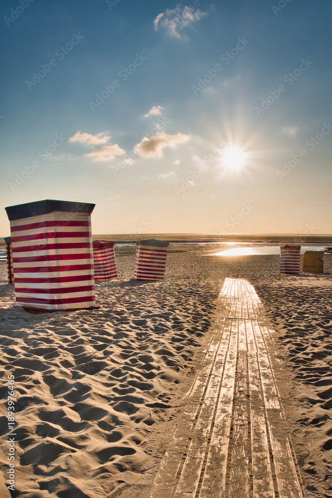 Fototapeta premium Traditional Striped Beach Tents on Borkum Island at Sunset with Wooden Path