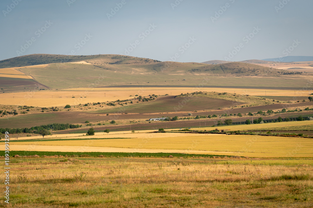 Fototapeta premium Wide landscape with rolling hills and fields in a rural area during daytime under a clear sky