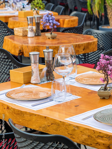 modern and elegant outdoor restaurant table setting with rustic wooden tables and stylish black chairs, ready for al fresco dining.