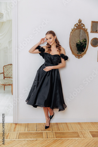 Portrait of a beautiful girl in a black evening dress near the wall