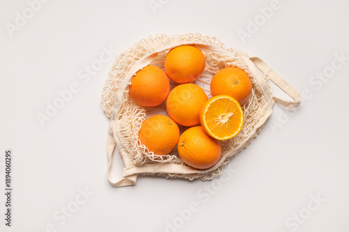 Mesh string bag with ripe oranges on gray background flat lay top view. Concept of reusable bag for shopping, goods, and eco-friendly living. Zero waste. Background with citrus fruits
