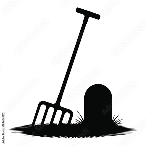 Silhouette of a garden pitchfork next to a tombstone in grass