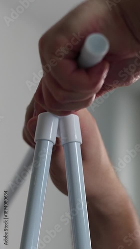 Vertical 4K video close up. 60 fps. Male hand inserting white metal pipe into plastic shelf. Decorating flat, process of assembling inexpensive cheap modern furniture, easy construction, hobby concept