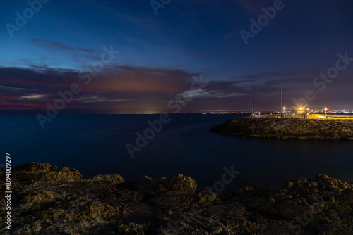 Fotografija Night seascape with rocky coast and distant city lights of Antalya on the horizon