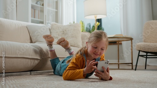 Fotografia Happy little girl with phone lying on floor Caucasian kid child daughter playing