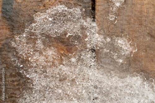 Ice bubbles and melting snow on wooden planks surface. Natural winter texture background. Macro shot. Cold season and thaw concept for design, poster, banner, wallpaper