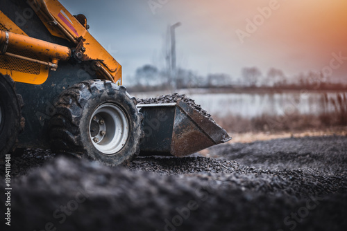 Mini loader with bucket. Mini loader is preparing the terrain. Mini wheel loader is spreading the stone onto the work surface.